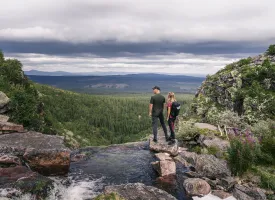 Ett ungt par står på toppen av et fossefall i Fulufjället og titter på utsikten.