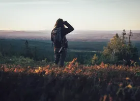 Een vrouw in een heuvelachtig landschap tuurt in de verte.