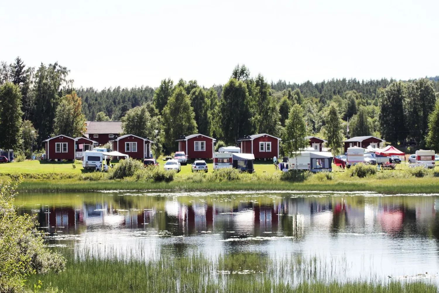 Utsikt over vannet mot røde campinghytter og campingvogner på Malungs camping.