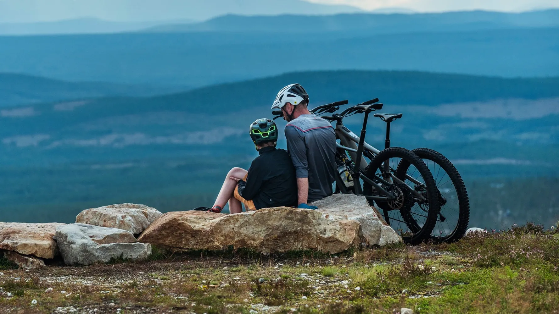 Far og sønn sitter på et fjell med MTB-syklene sine.