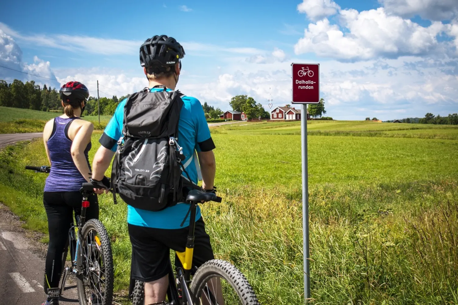 Twee mensen op mountainbikes kijken uit over een akker met een rood huis op de achtergrond.