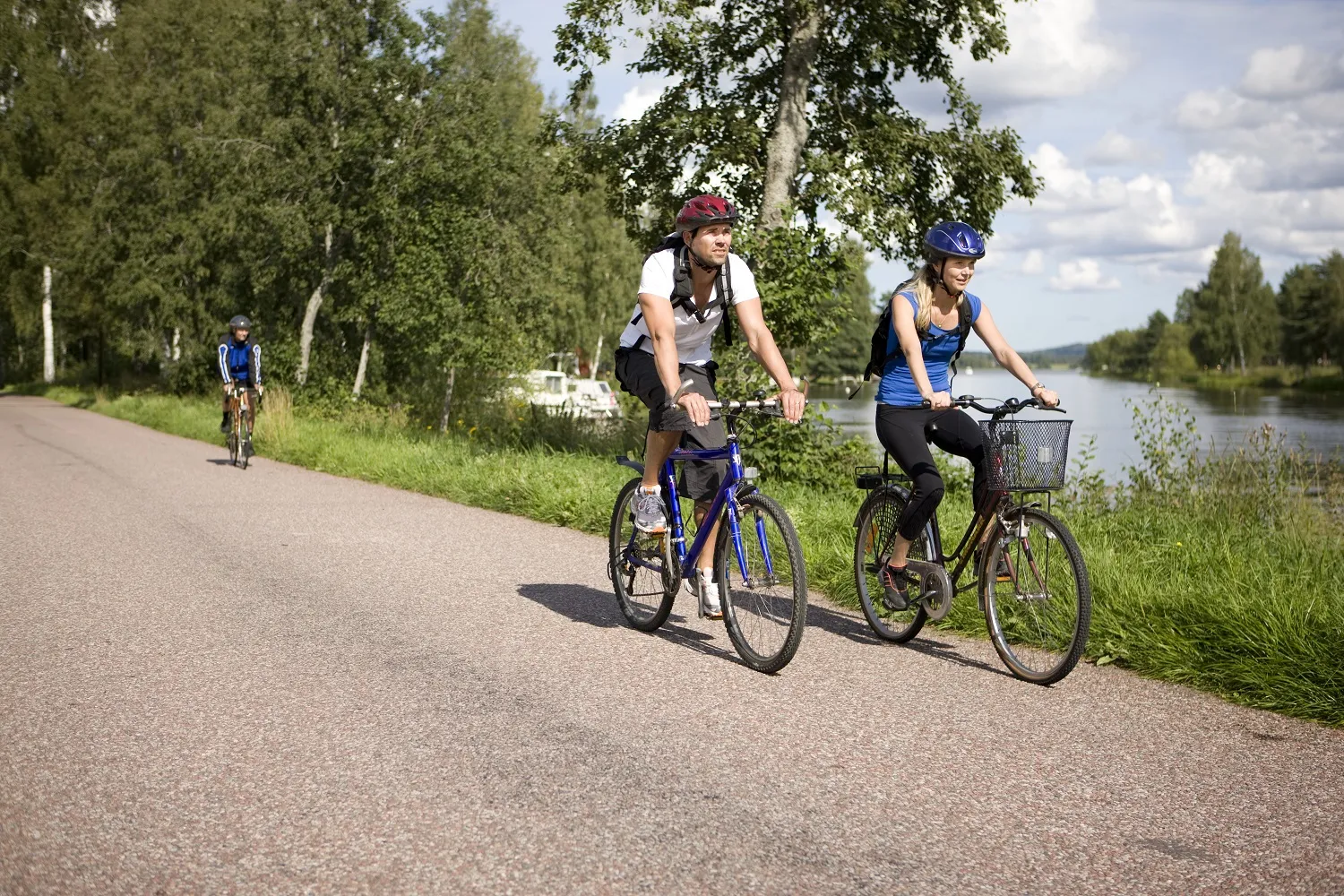 Twee mensen fietsen op een verharde weg met een meer op de achtergrond.