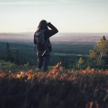 Een vrouw in een heuvelachtig landschap tuurt in de verte.