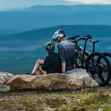 Far og sønn sitter på et fjell med MTB-syklene sine.