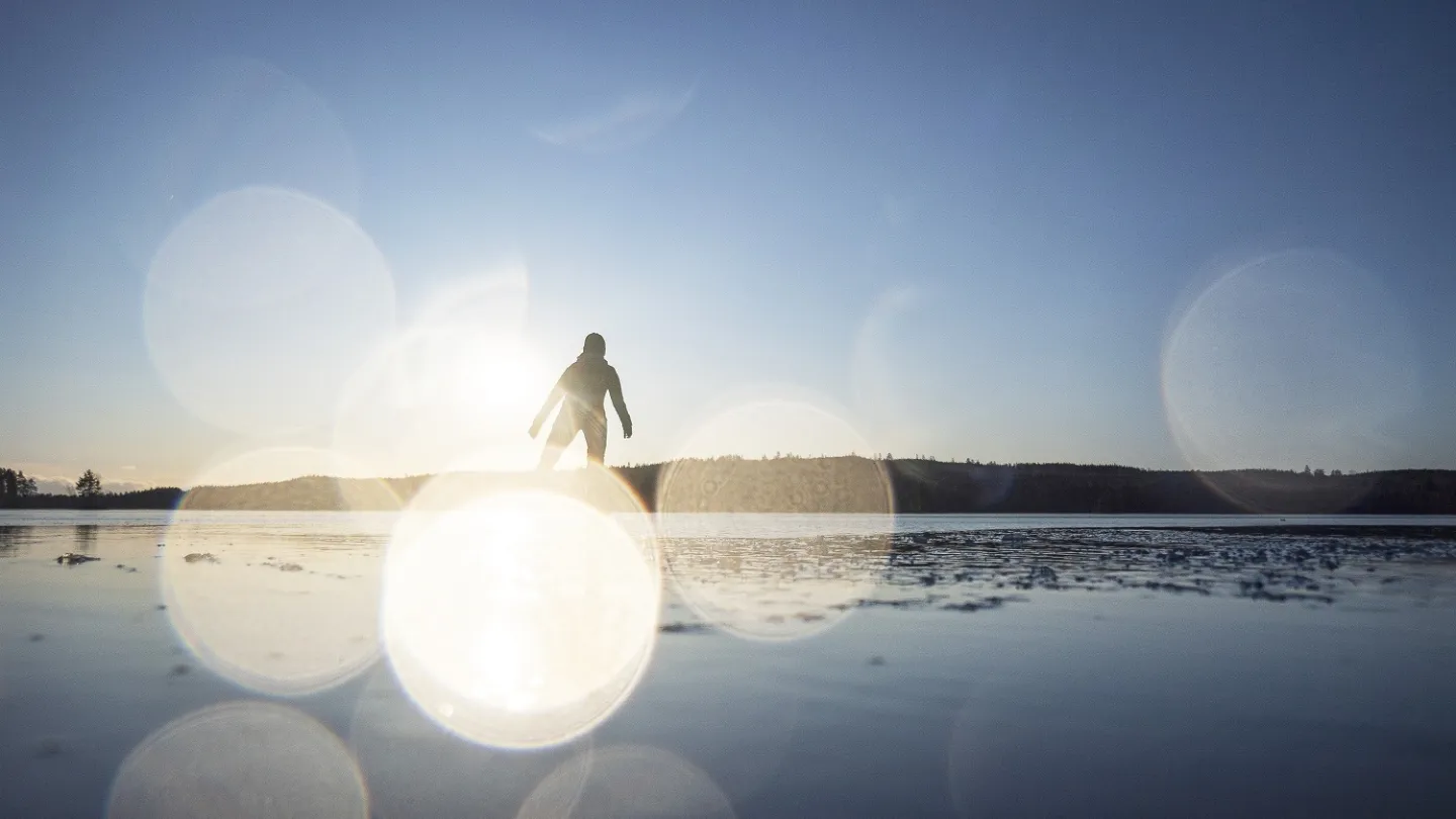 Een schaatser op natuurijs met fonkelingen van de zon.